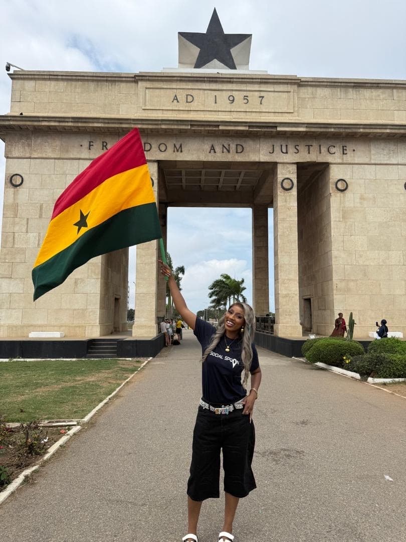 A Social Spoon team member holding the Ghana flag in front of Independence Arch in Accra